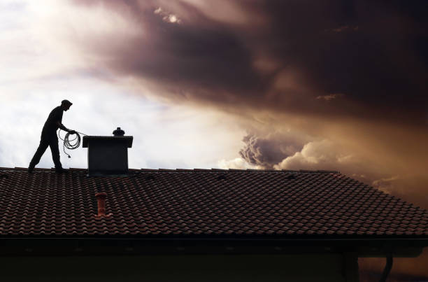 a chimney sweep cleans the chimney on a house roof while thunderclouds gather a chimney sweep cleans the chimney on a house roof while thunderclouds gather